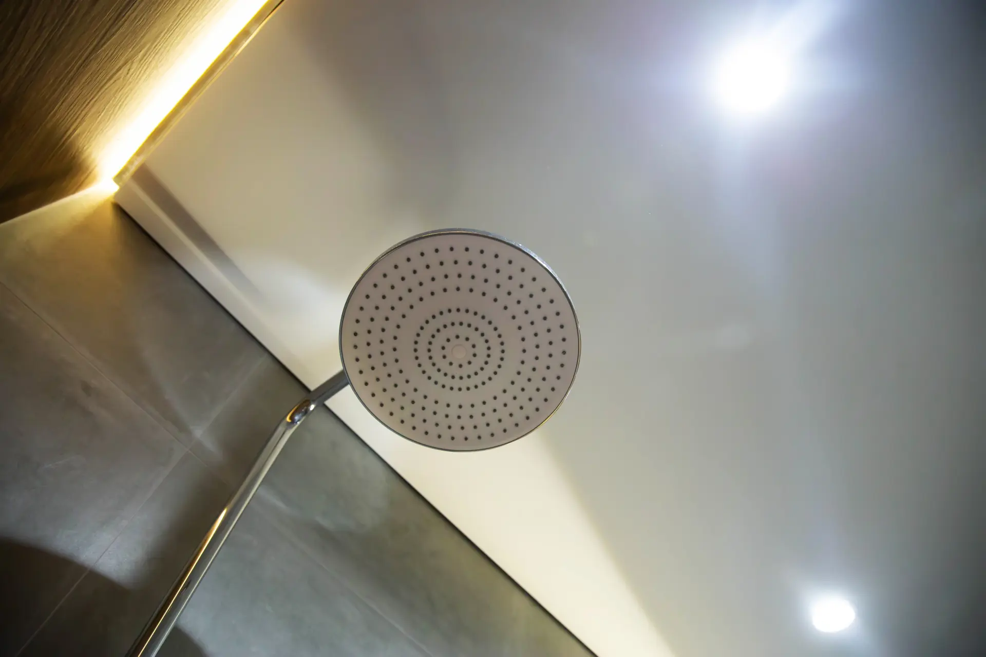 Detail okrúhlej dažďovej sprchy pod bielym napínacím stropom s bodovým LED osvetlením.