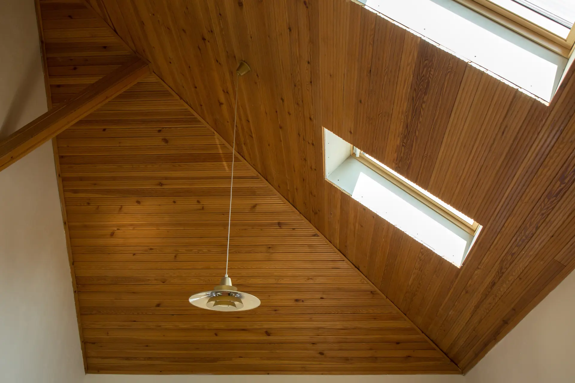 Drevený obklad stropu so strešnými oknami a závesným svietidlom.