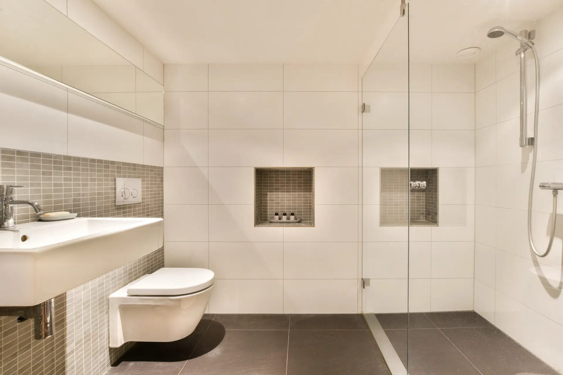 Minimalistická kúpeľňa s walk-in sprchou, závesným WC a svetlými obkladmi s úložnými nikami.