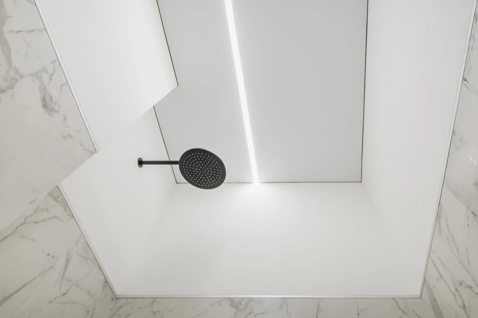 Napínaný strop v modernej kúpeľni s líniovým LED osvetlením a zapustenou sprchovou hlavicou v minimalistickom dizajne.