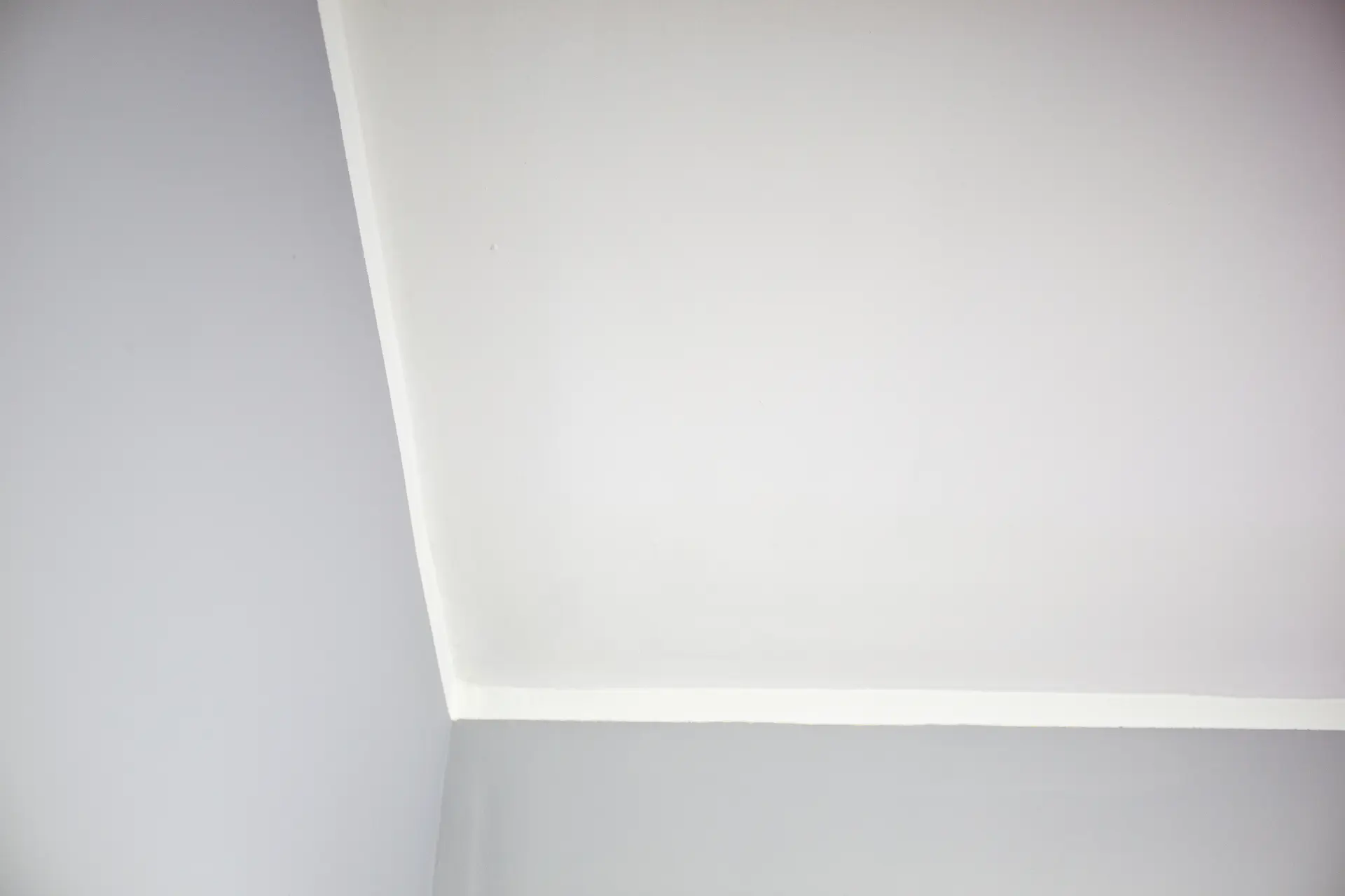 Biely napínaný strop s jemným obvodovým LED osvetlením v rohu miestnosti, vytvárajúci čistý a moderný vzhľad interiéru.
